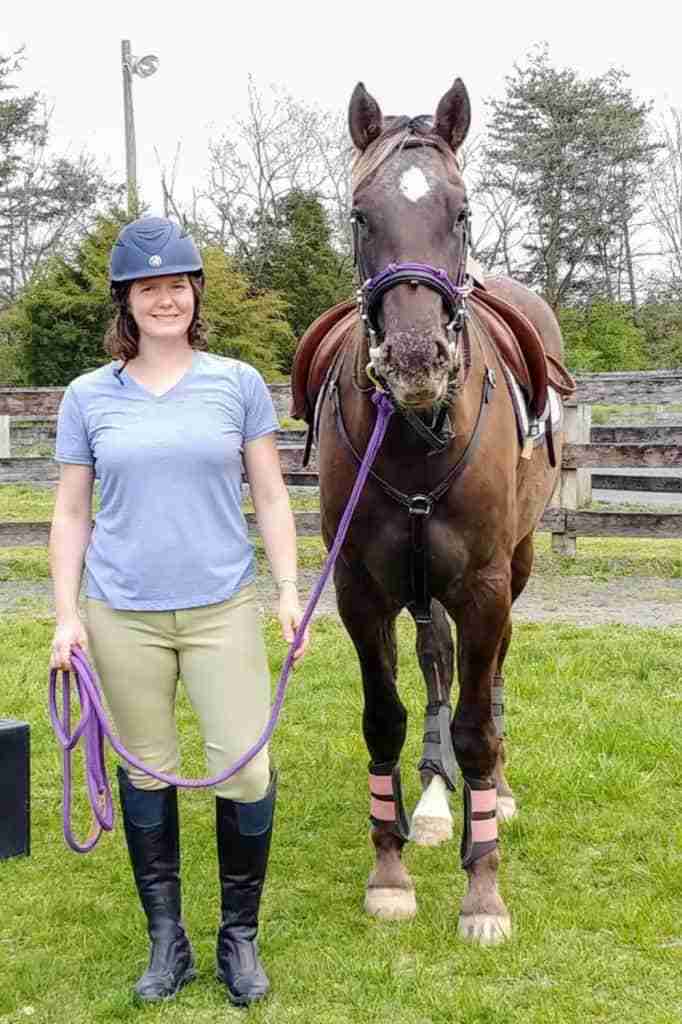 Woman in english horseback riding clothes standing next to a brown horse with a white star.