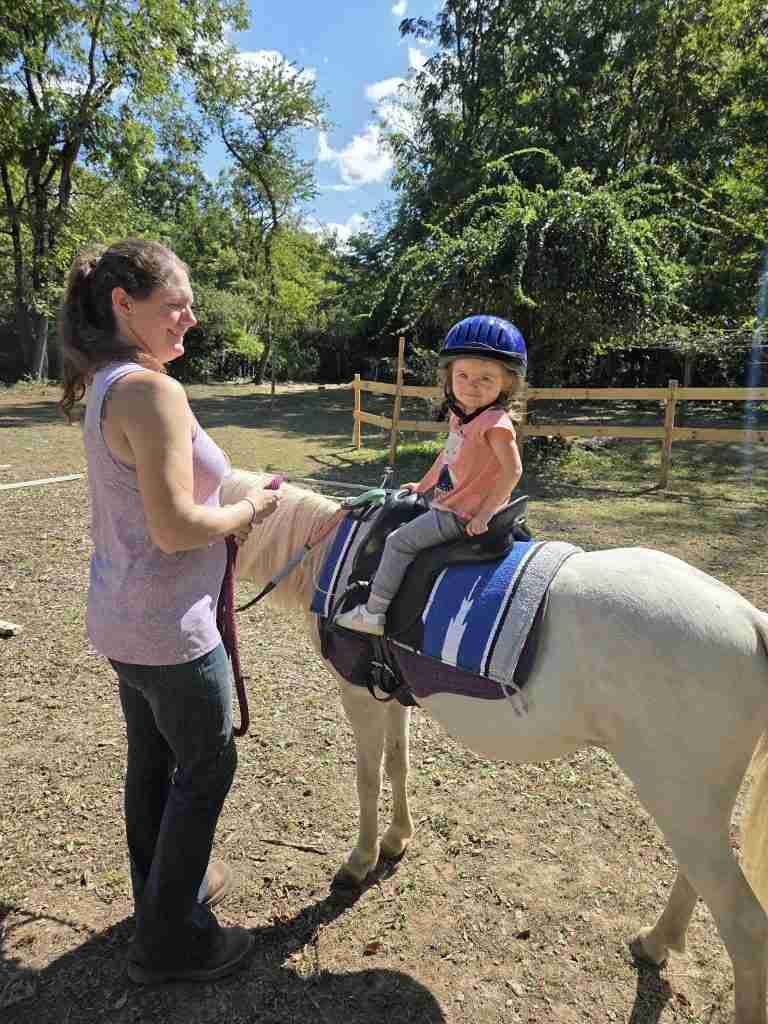 Brunette standing facing a child riding a white pony.