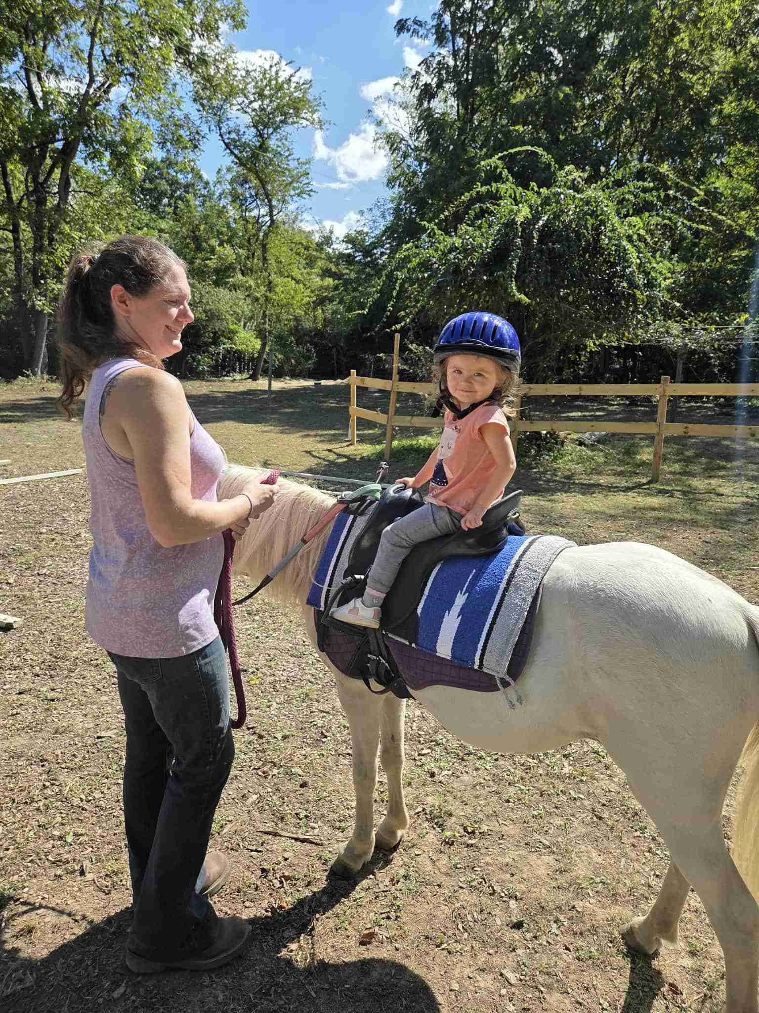 Brunette standing facing a child riding a white pony.