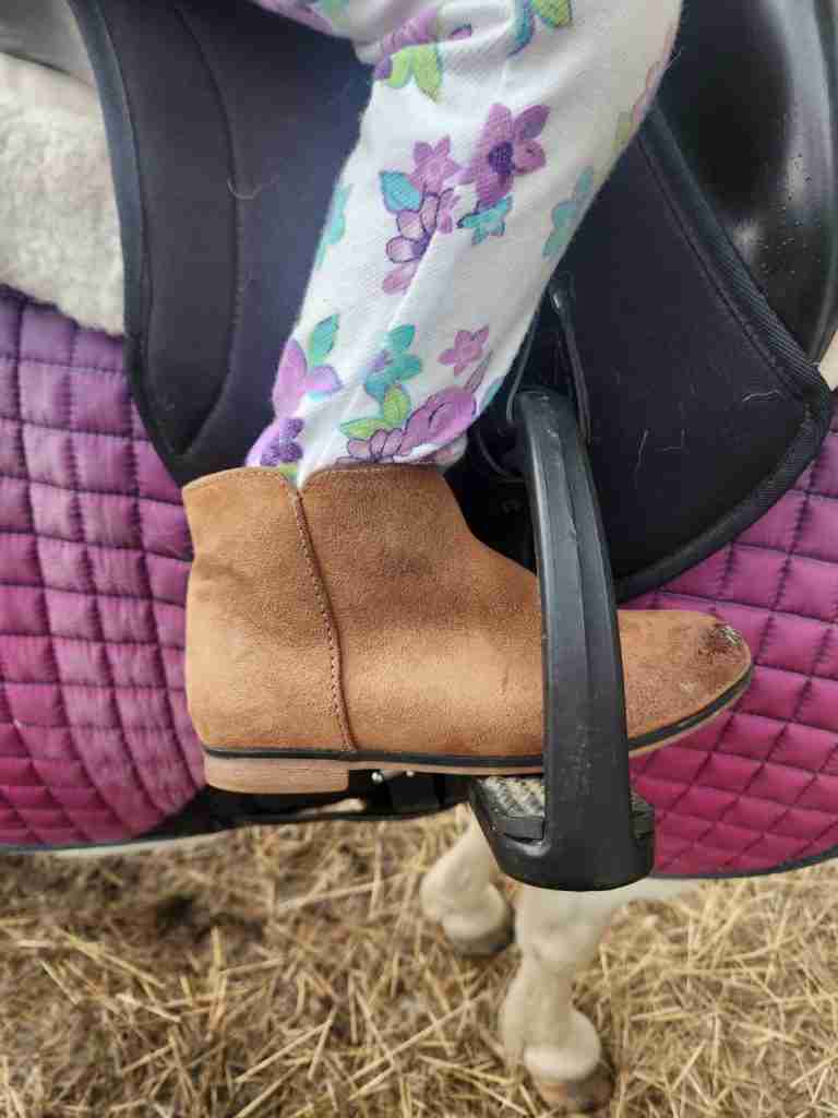 Cat & Jack boot in a stirrup with a purple saddle pad and black saddle behind it.